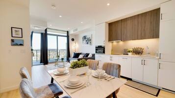 A modern kitchen with white cabinets, a dining area with a table set for four, and a view of the city through large windows.