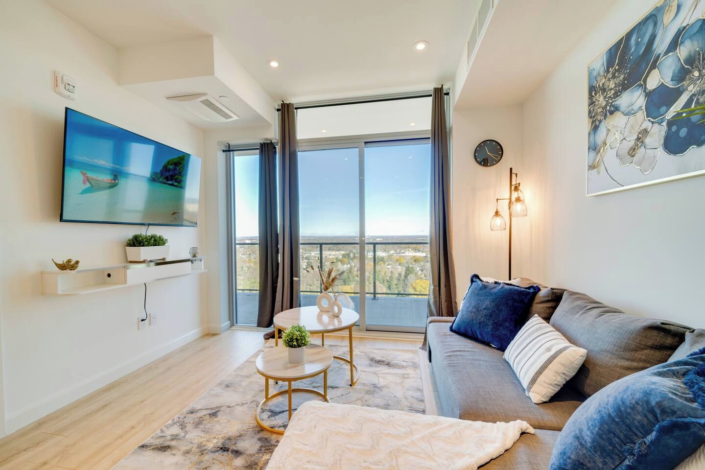 Una sala de estar moderna con un televisor de pantalla plana, un sofá con cojines azules, una mesa de centro redonda y un ventanal con cortinas.