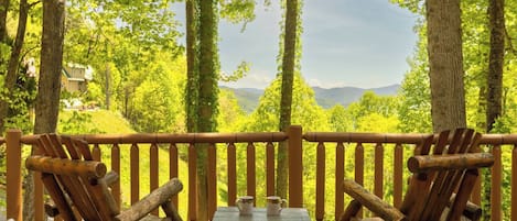 A wooden deck with two rocking chairs and a small table, overlooking a forested landscape.