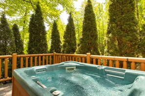 Ein Whirlpool mit Holzgeländer, umgeben von hohen Bäumen.