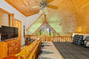 A cozy attic bedroom with a wooden ceiling, a large window, a bed, a TV, and a wooden dresser. - Little Bear Chalet - Mtn Views/Hot Tub/EV Charger (Bryson City)