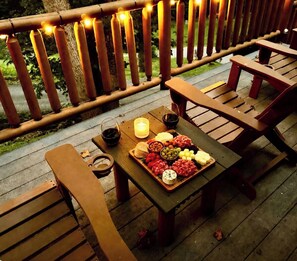 A wooden deck with a table set for a meal, featuring a charcuterie board, glasses of wine, and a candle. - Little Bear Chalet - Mtn Views/Hot Tub/EV Charger (Bryson City)