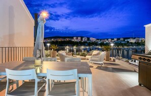 Eine Außenpatio mit Esstisch und Stühlen, einem Grill und Blick auf eine Stadtlandschaft in der Dämmerung.