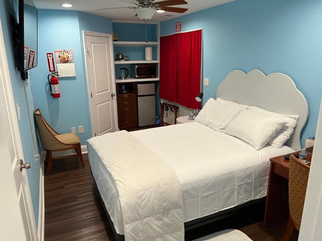 Un dormitorio con cama, una silla, un escritorio, un microondas y una cortina roja.