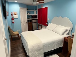 Un dormitorio con cama, una silla, un escritorio, un microondas y una cortina roja.