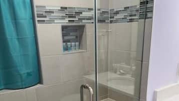 A glass-enclosed shower with a tiled floor, a metal handle, and a small shelf with toiletries.