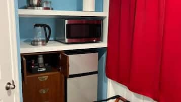 A compact kitchen with a microwave, kettle, and storage drawers.