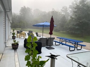 Um pátio externo com assentos, uma mesa e um guarda-sol azul.
