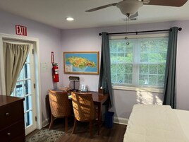 Habitación de hotel con cama, escritorio con sillas, mapa en la pared, señal de salida y ventana con cortinas.