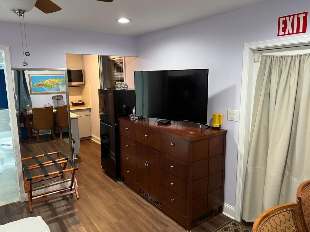 Habitación de hotel con cómoda de madera, televisor de pantalla plana, zona de comedor con sillas y señal de salida.