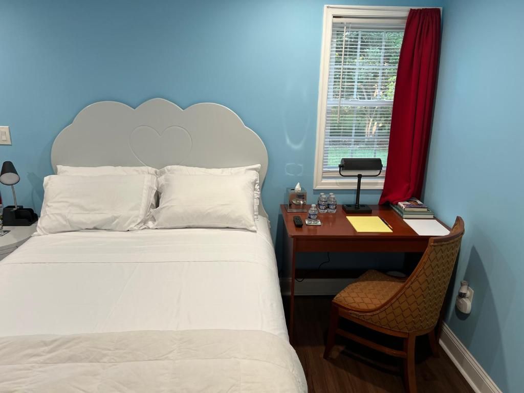 Une chambre à coucher avec un lit, un bureau, une chaise, une fenêtre avec des stores et un rideau rouge.
