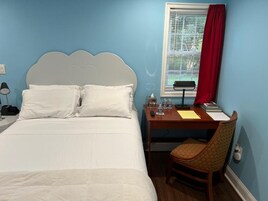 Un dormitorio con una cama, un escritorio, una silla, un ventanal con persianas y una cortina roja.