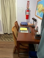 Una habitación con un escritorio de madera, una silla, un extintor, un mapa en la pared y una alfombra de bienvenida.