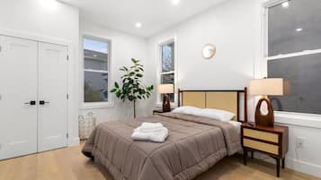Une chambre à coucher avec un lit, des tables de chevet, une plante et une fenêtre.