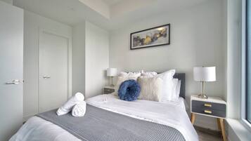 A hotel room with a bed, a bedside table with a lamp, a wall-mounted painting, and a window.