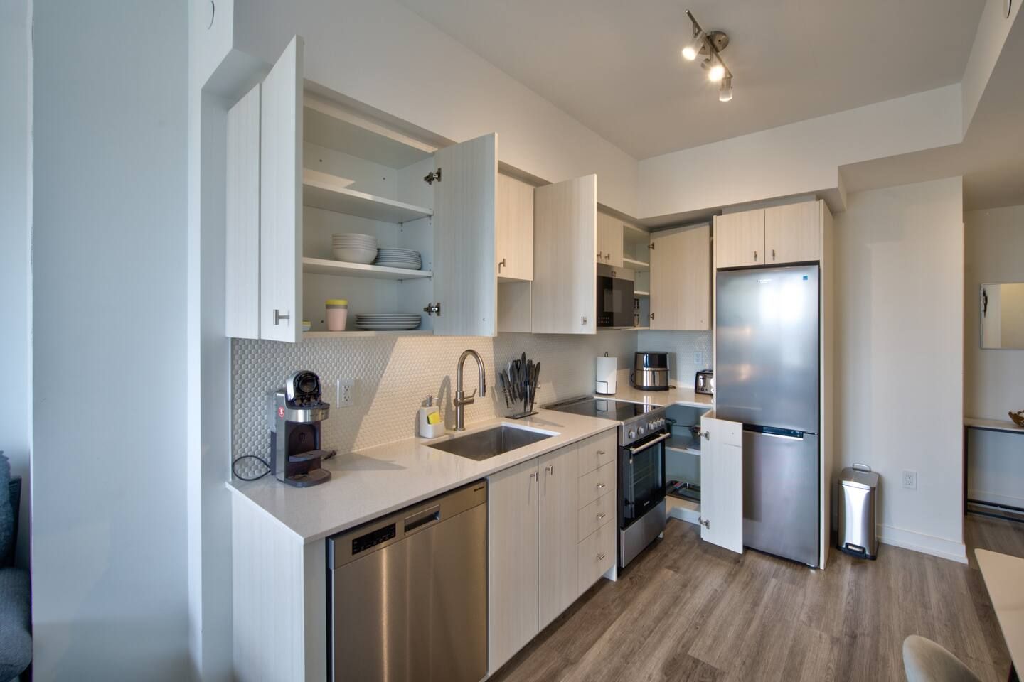 Una cocina moderna con electrodomésticos de acero inoxidable, armarios blancos y lavavajillas integrado.