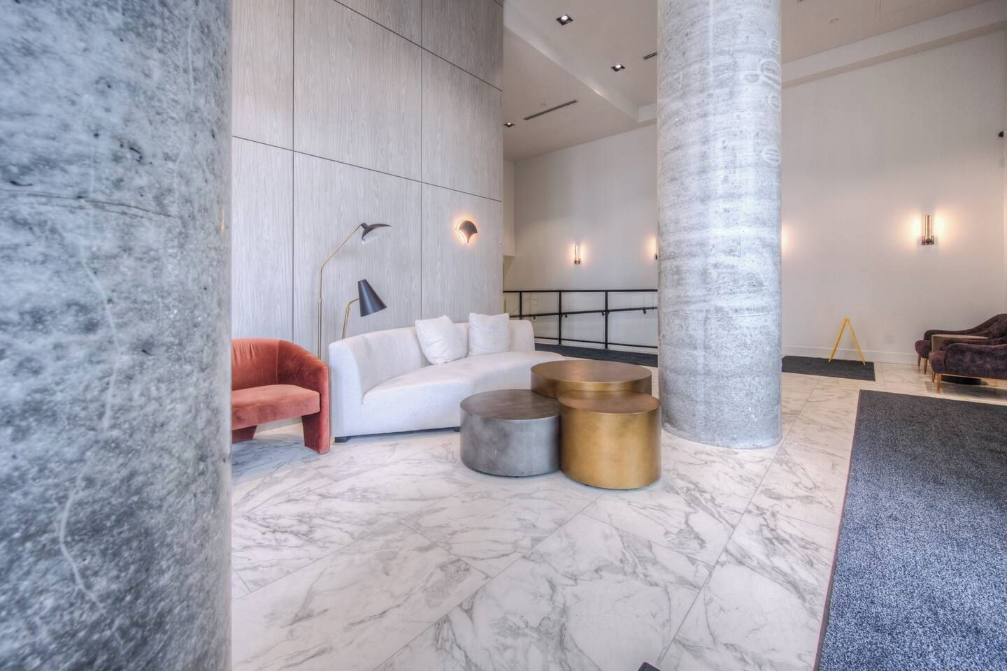A modern lobby with marble flooring, a white sofa, a red armchair, and a large pillar.