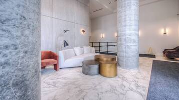 A modern lobby with marble flooring, a white sofa, a red armchair, and a large pillar.