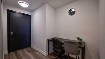 A room with a dark door, a desk with a chair, a small plant, and a wall clock.