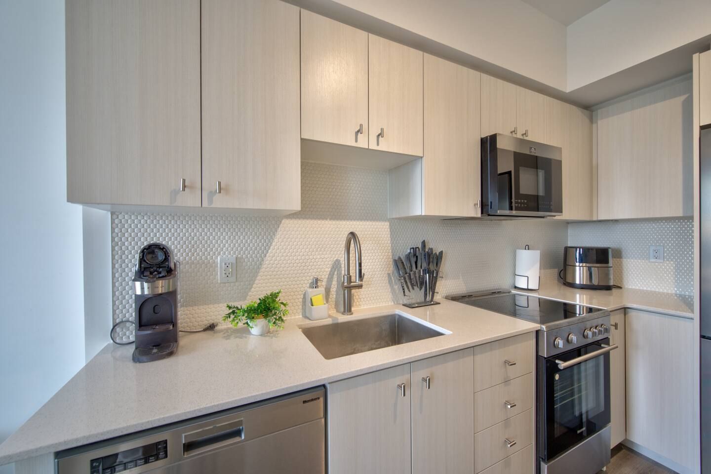 A modern kitchen with light wood cabinets, stainless steel appliances, and a white countertop.