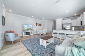 A modern living room with a flat-screen TV, a dining area, and a kitchen with white cabinets. - 3-bedroom townhome in perfect Orange Beach with AC (Orange Beach)