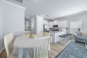 A modern kitchen with white cabinetry, a dining area with a round table, and a living space with a grey sofa. - 3-bedroom townhome in perfect Orange Beach with AC (Orange Beach)