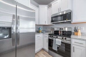 A modern kitchen with stainless steel appliances, white cabinetry, and a granite countertop. - 3-bedroom townhome in perfect Orange Beach with AC (Orange Beach)