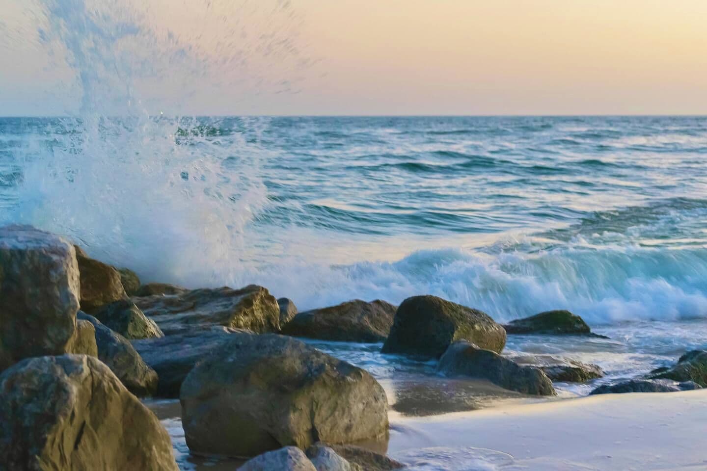 A beach with waves crashing against large rocks and a clear view of the ocean.