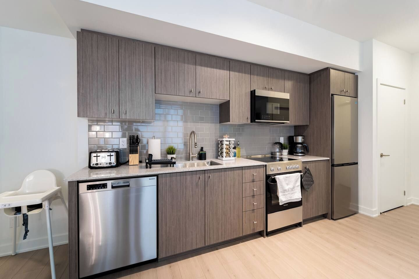 A modern kitchen with grey cabinetry, stainless steel appliances, and a white countertop.