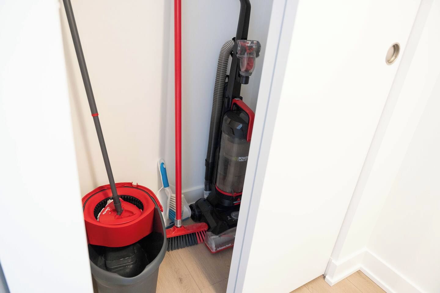 A narrow hallway with a mop, broom, and vacuum cleaner.