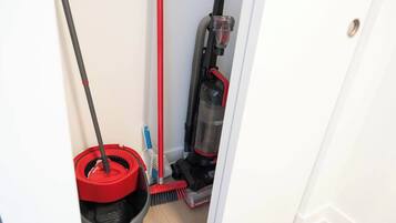 A narrow hallway with a mop, broom, and vacuum cleaner.