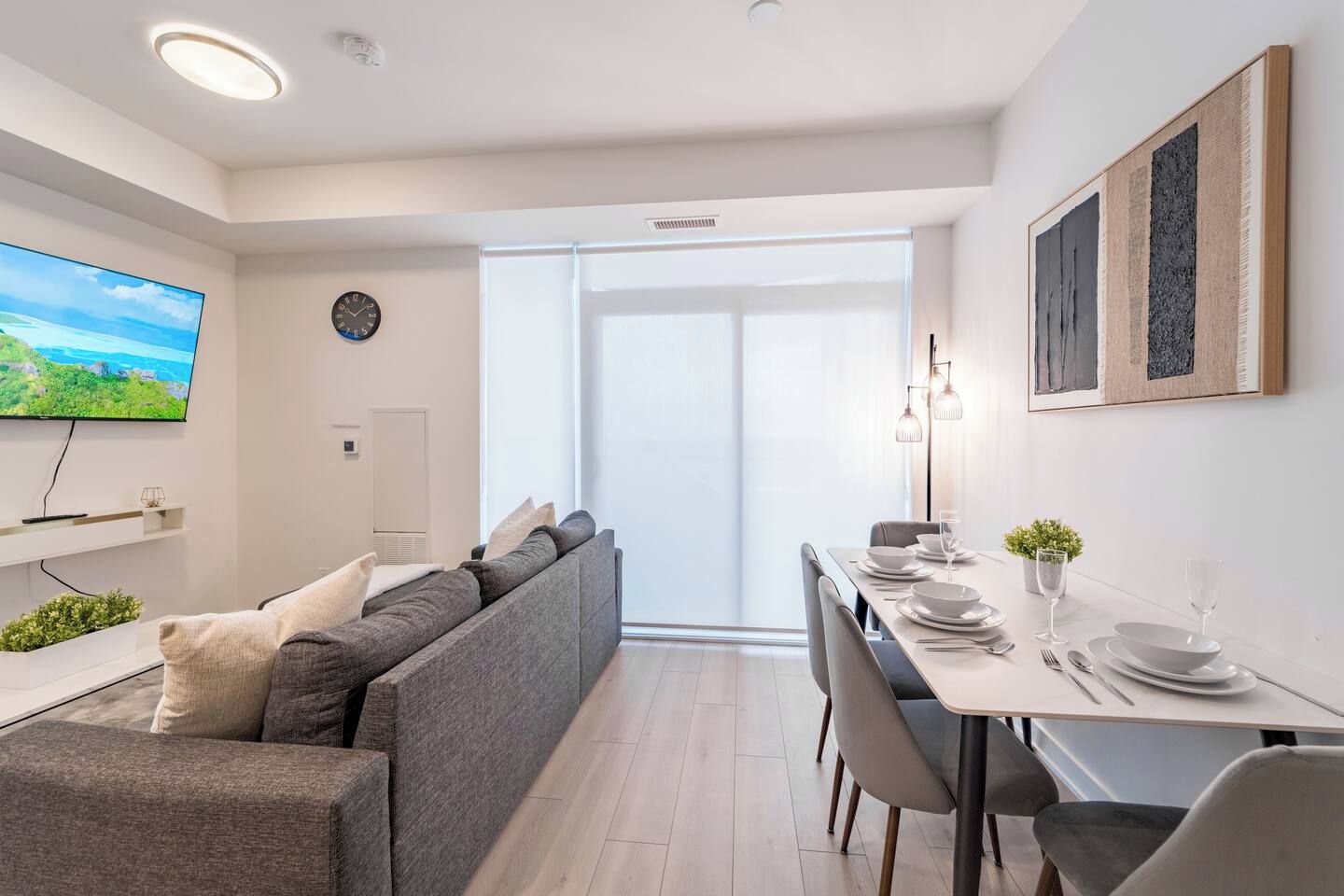 En moderne stue med en sofa, et spisebord dækket til to personer og et fjernsyn ophængt på væggen.