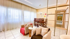 A modern living room with a sofa, armchairs, a coffee table, and a dining area with chairs and a table. - Apartment with Balcony and Parking near Porto da Barra Beach (Salvador)