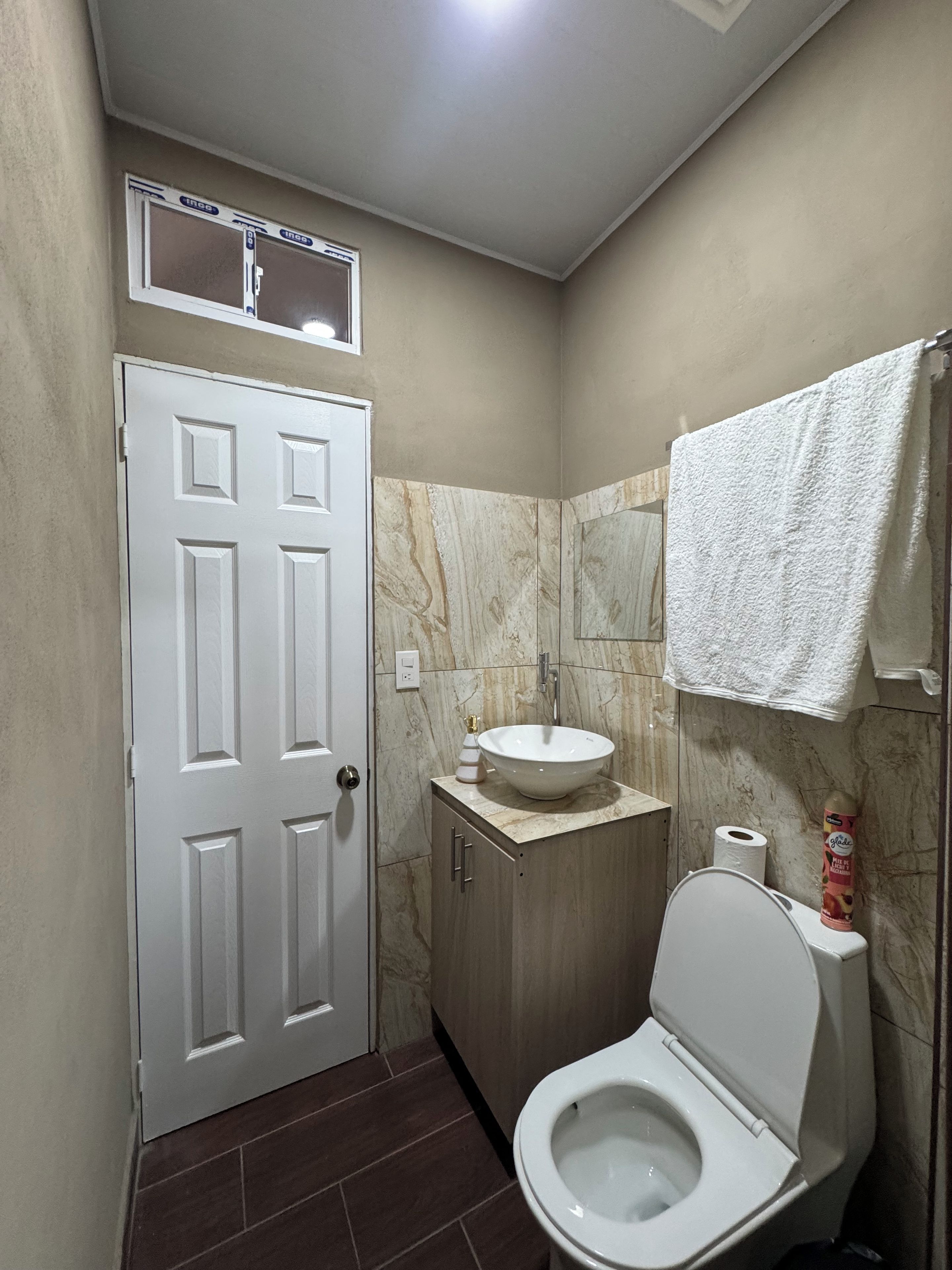 Une salle de bain avec des toilettes, un lavabo, une serviette accrochée au mur et une porte.