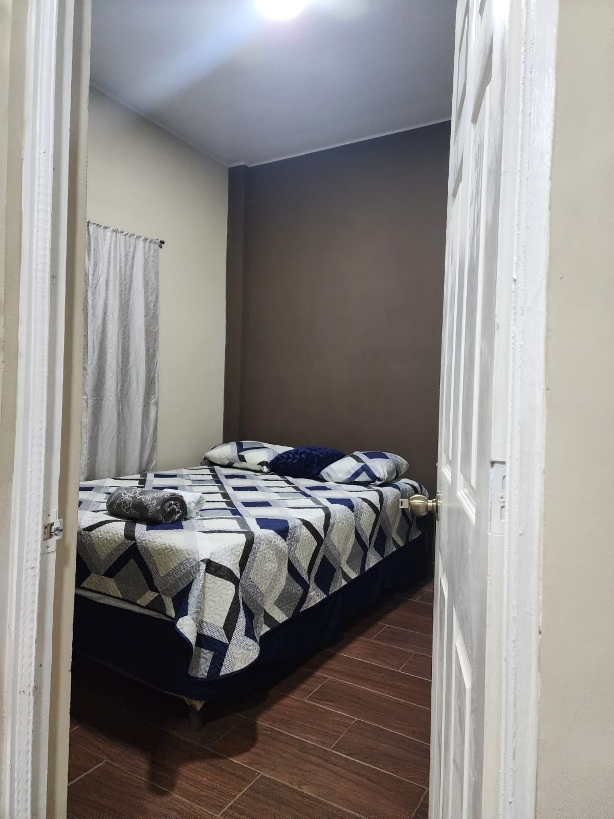 A small, narrow room with a bed, a curtain, and a door.