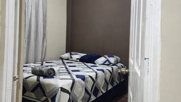 A small, narrow room with a bed, a curtain, and a door.