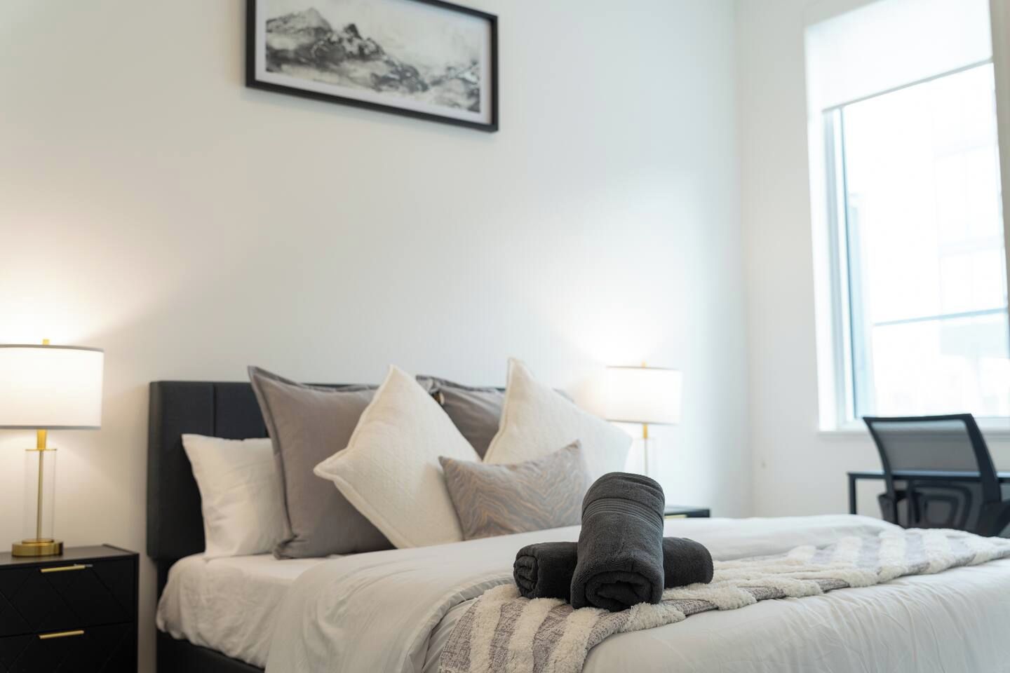 Una cama bien hecha con almohadas y una colcha, una mesita de noche con una lámpara y un cuadro en la pared.