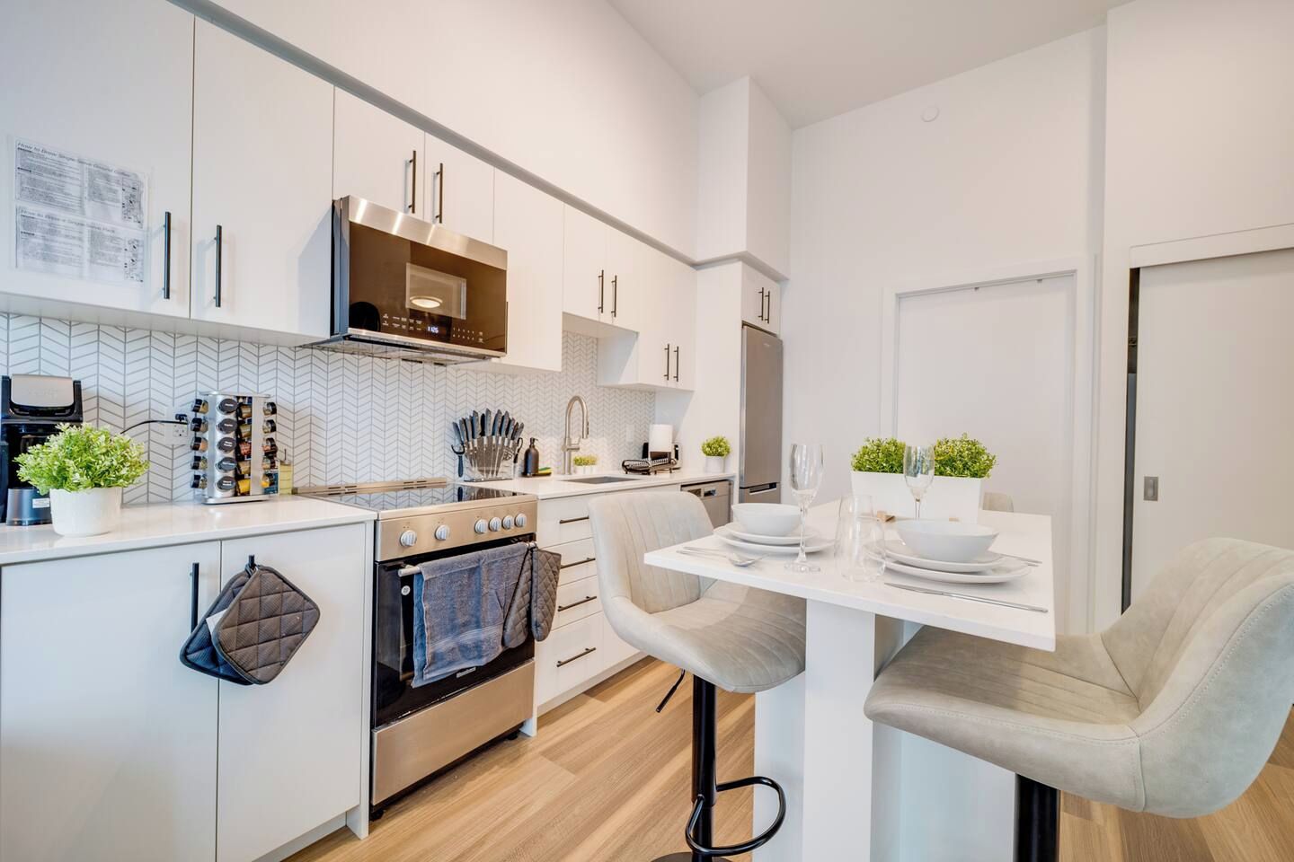 A modern kitchen with white cabinetry, a built-in oven, and a dining area with a table set for two.
