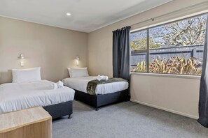 A hotel room with two beds, a small wooden table, and a window with curtains. - Rainbow Haven, Walk to the Lake (Taupō)