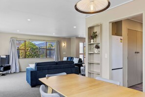 A modern living room with a sofa, a dining table, and a kitchen area with a refrigerator. - Rainbow Haven, Walk to the Lake (Taupō)