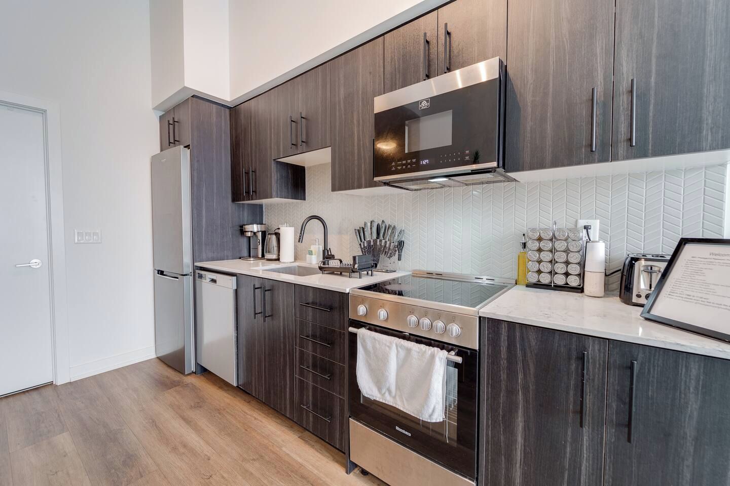 Una cocina moderna con armarios de madera oscura, electrodomésticos de acero inoxidable y salpicadero de azulejos blancos.
