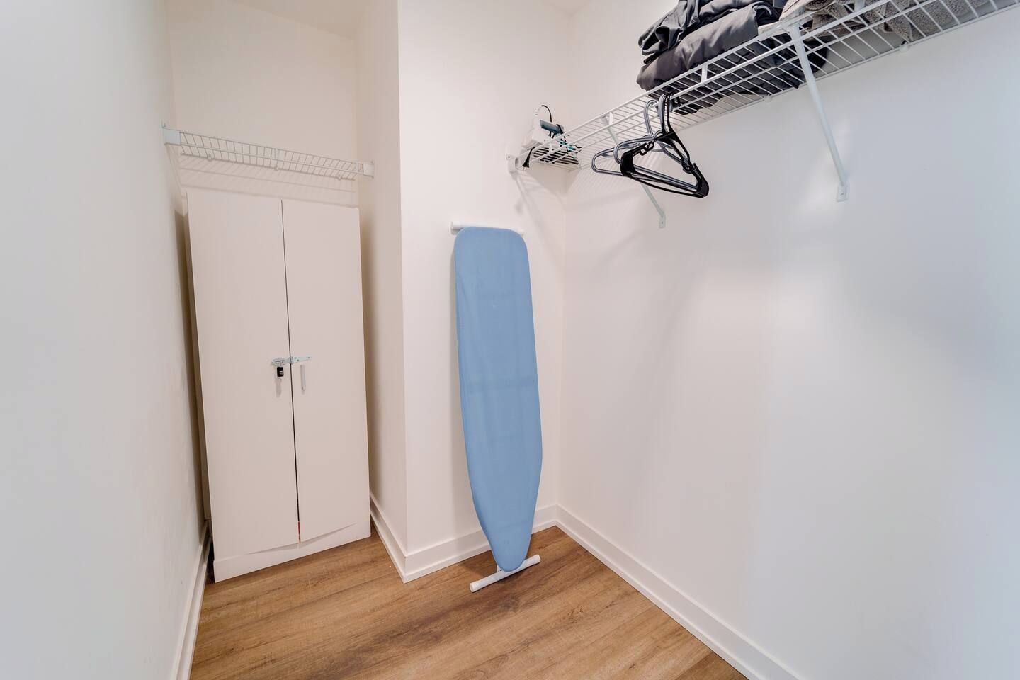 Ein Flur mit einem weißen Kleiderschrank, einem blauen Bügelbrett und einem Wäscheständer an der Wand.