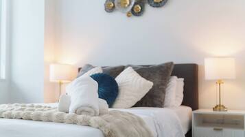 Een keurig opgemaakt bed met een zachte, witte deken, een blauw kussen en een wit kussen. Twee nachtkastjes met lampen staan aan weerszijden van het bed.
