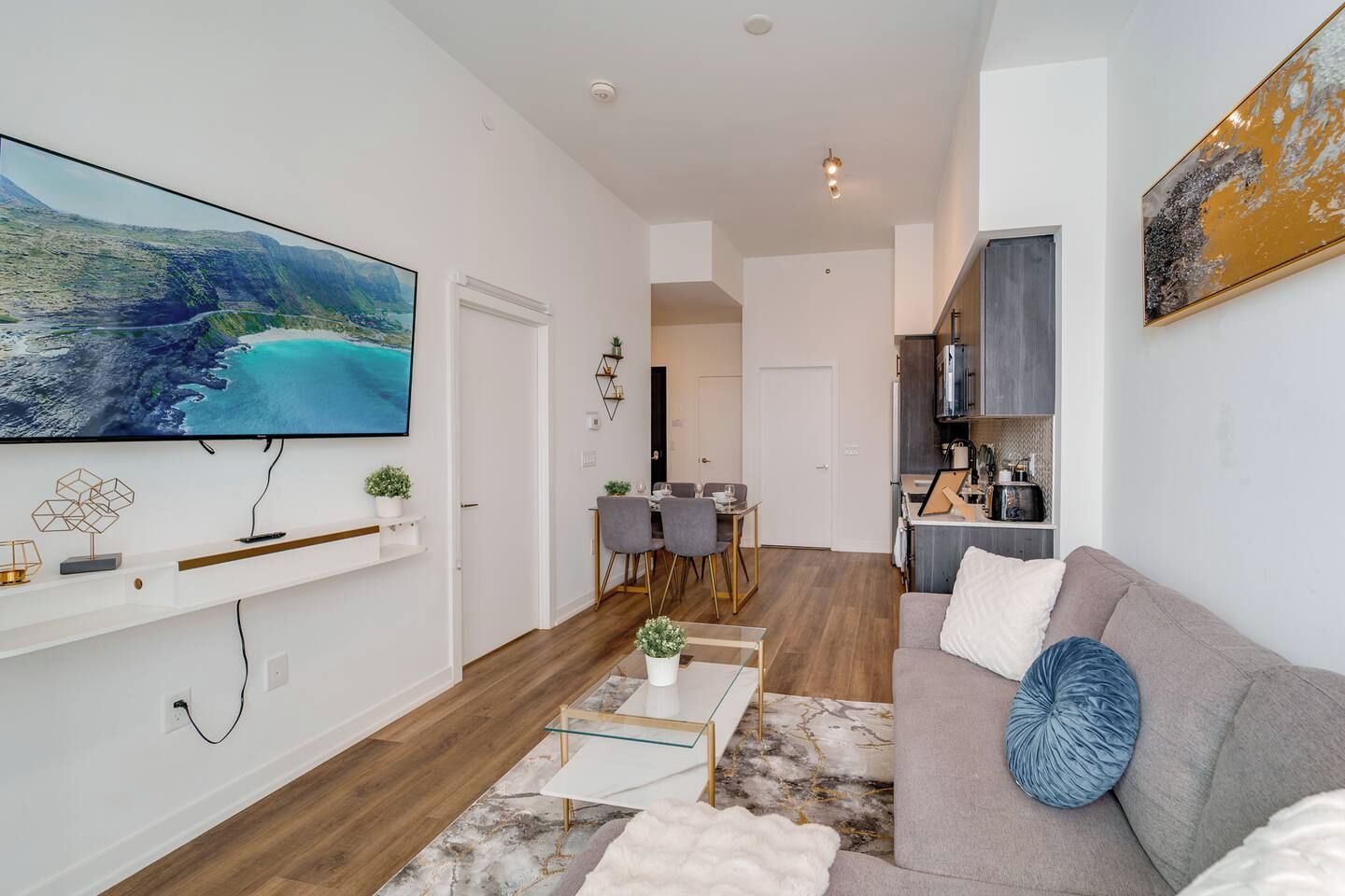 A modern living room with a flat-screen TV, a sofa, a dining area, and a kitchen.