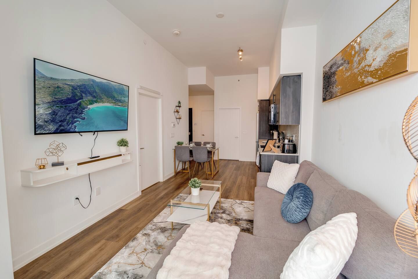 A modern living room with a flat-screen TV, a sofa, a coffee table, and a dining area with chairs.