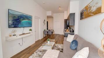 A modern living room with a flat-screen TV, a sofa, a coffee table, and a dining area with chairs.