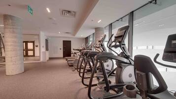 A row of stationary bikes in a well-lit indoor space with a concrete pillar, a door, and a glass wall.