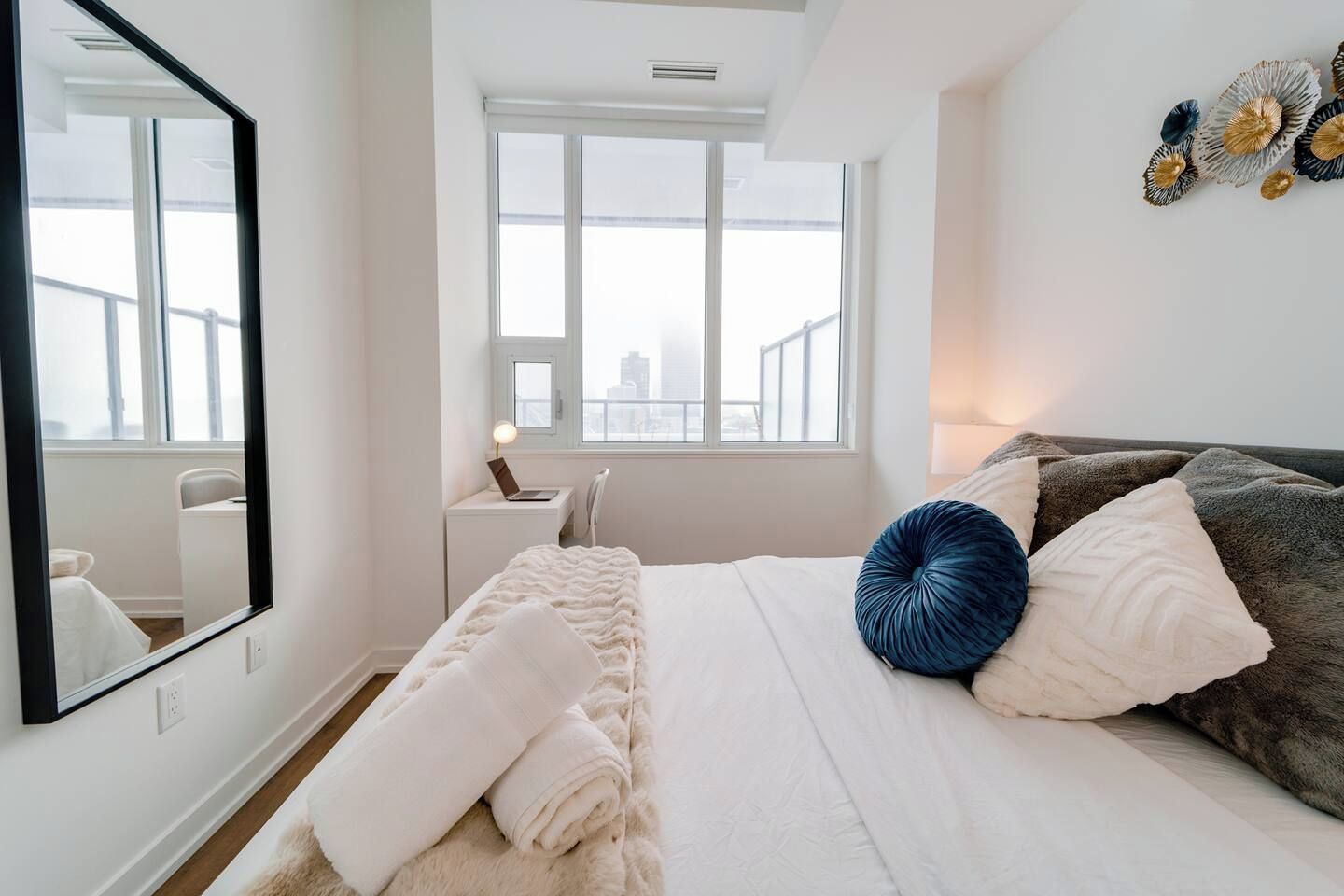 Un dormitorio con cama, escritorio, silla, ventana y espejo.
