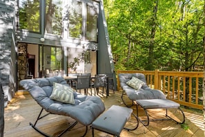 Une terrasse dotée de deux fauteuils à bascule gris, d’une table et de chaises, le tout entouré d’une terrasse en bois et d’un mur en pierre.