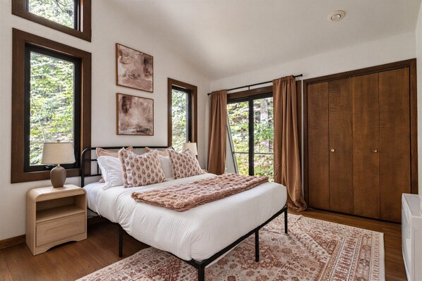A bedroom with a bed, nightstands, a lamp, a large window, and a wardrobe.